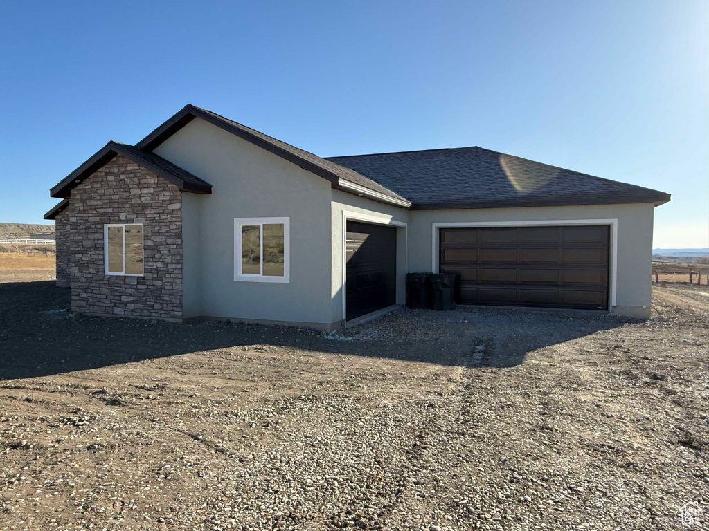 Ranch-style home with stucco siding, stone siding, an attached garage, and driveway