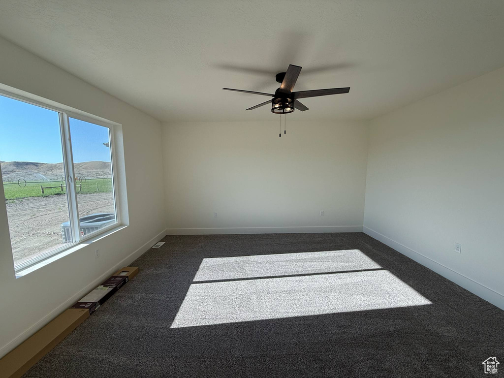 Empty room featuring a ceiling fan, dark carpet, and baseboards