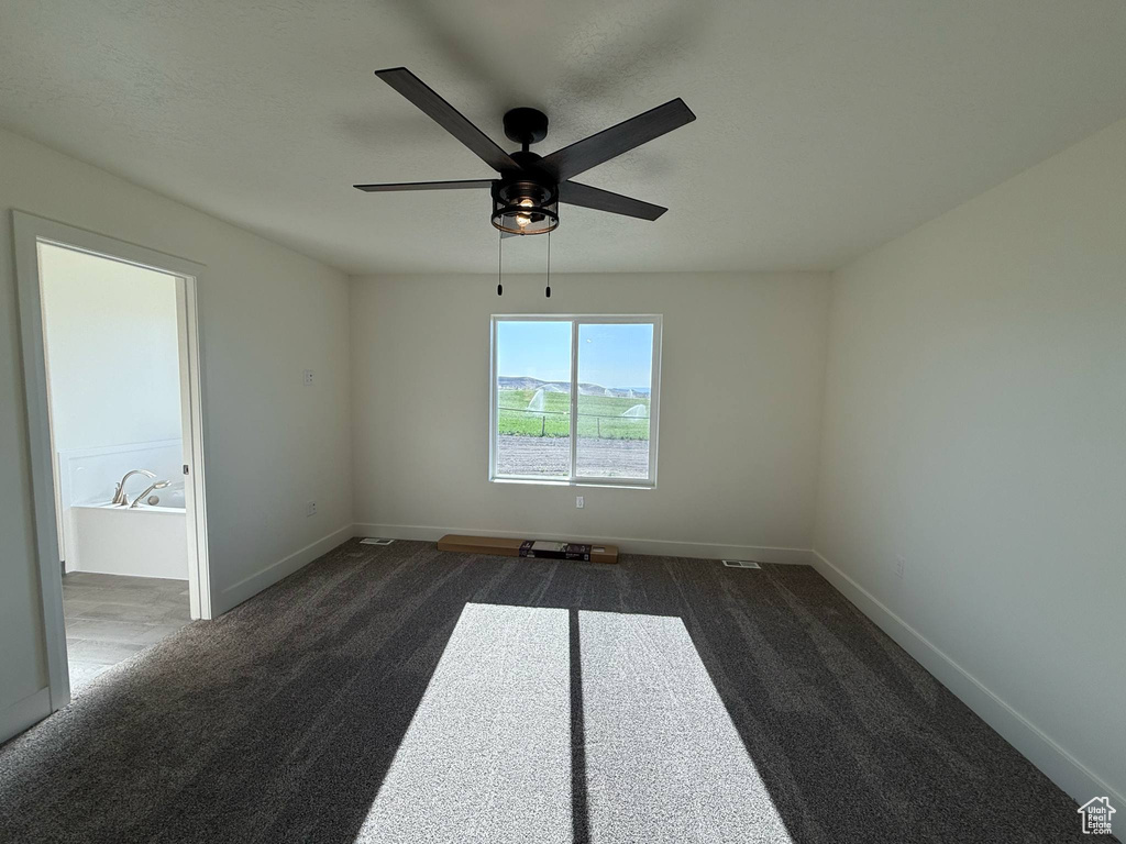 Empty room featuring dark carpet, a ceiling fan, and baseboards