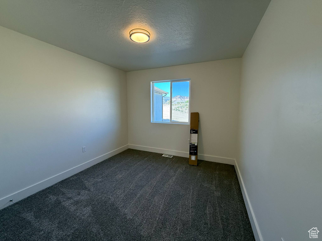 Spare room featuring baseboards, dark colored carpet, and a textured ceiling