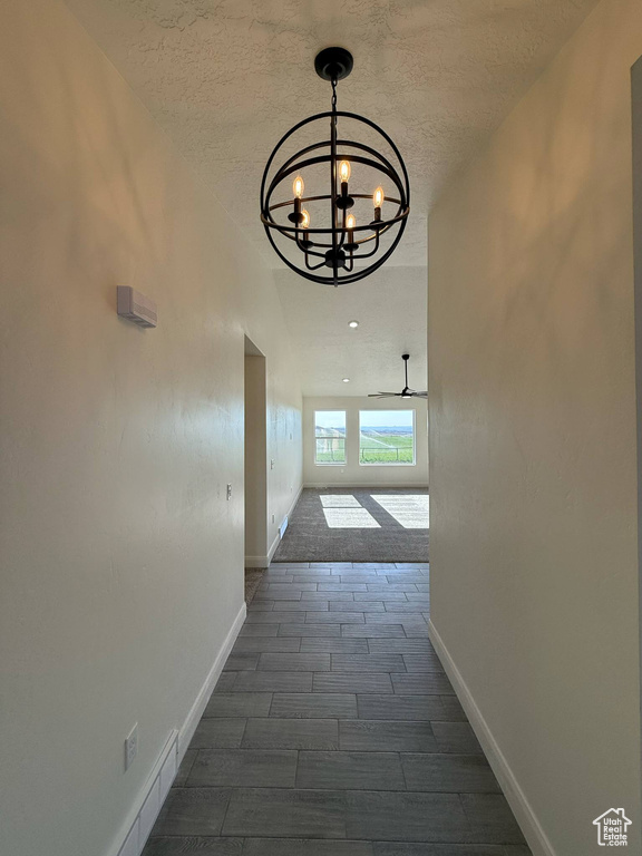Hall with a chandelier, a textured ceiling, baseboards, and wood tiled floors