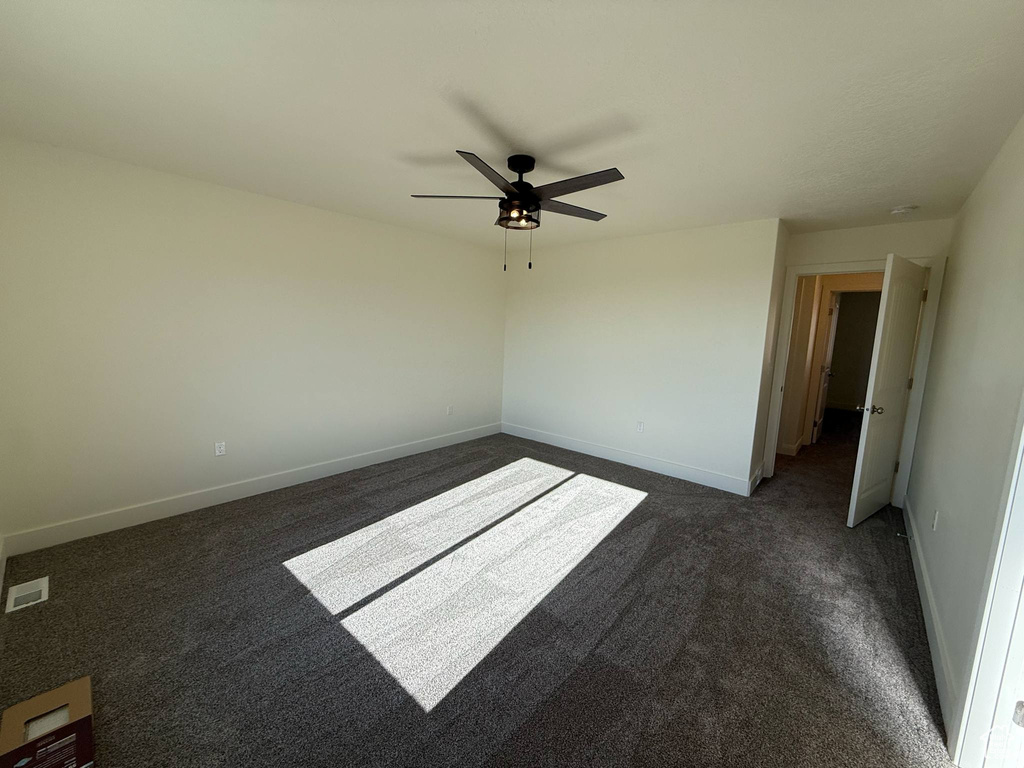 Empty room with dark colored carpet, a ceiling fan, and baseboards