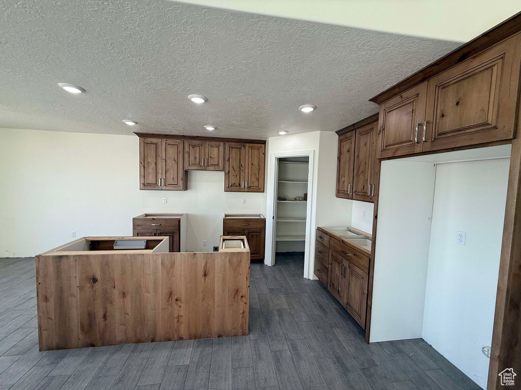 Kitchen featuring brown cabinetry, dark wood finished floors, recessed lighting, a textured ceiling, and a center island