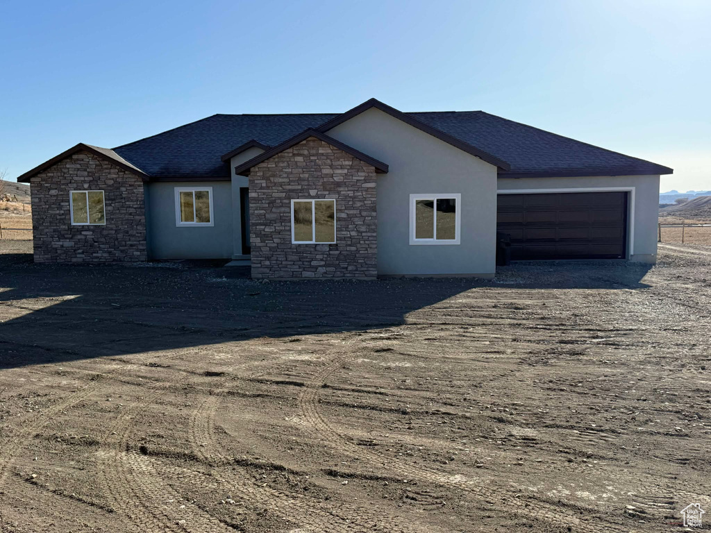 Single story home with stone siding, stucco siding, a shingled roof, and a garage