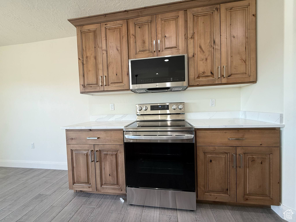 Kitchen with stainless steel appliances, brown cabinetry, light wood-style flooring, baseboards, and a textured ceiling
