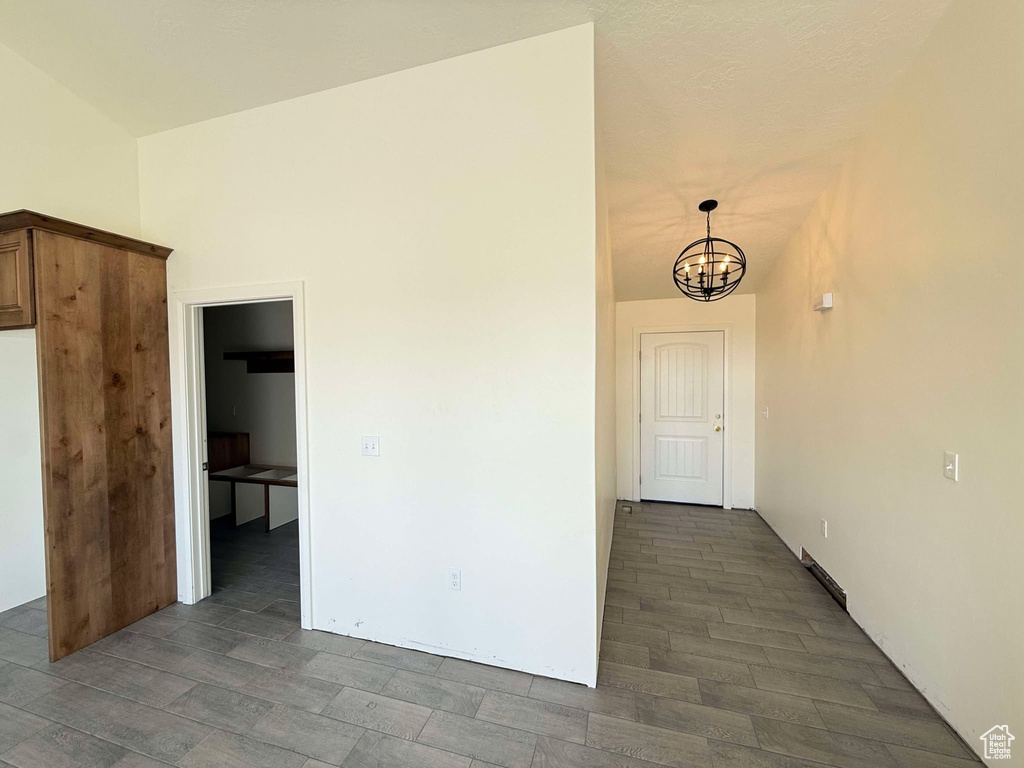 Empty room with vaulted ceiling, dark wood-style flooring, and a chandelier