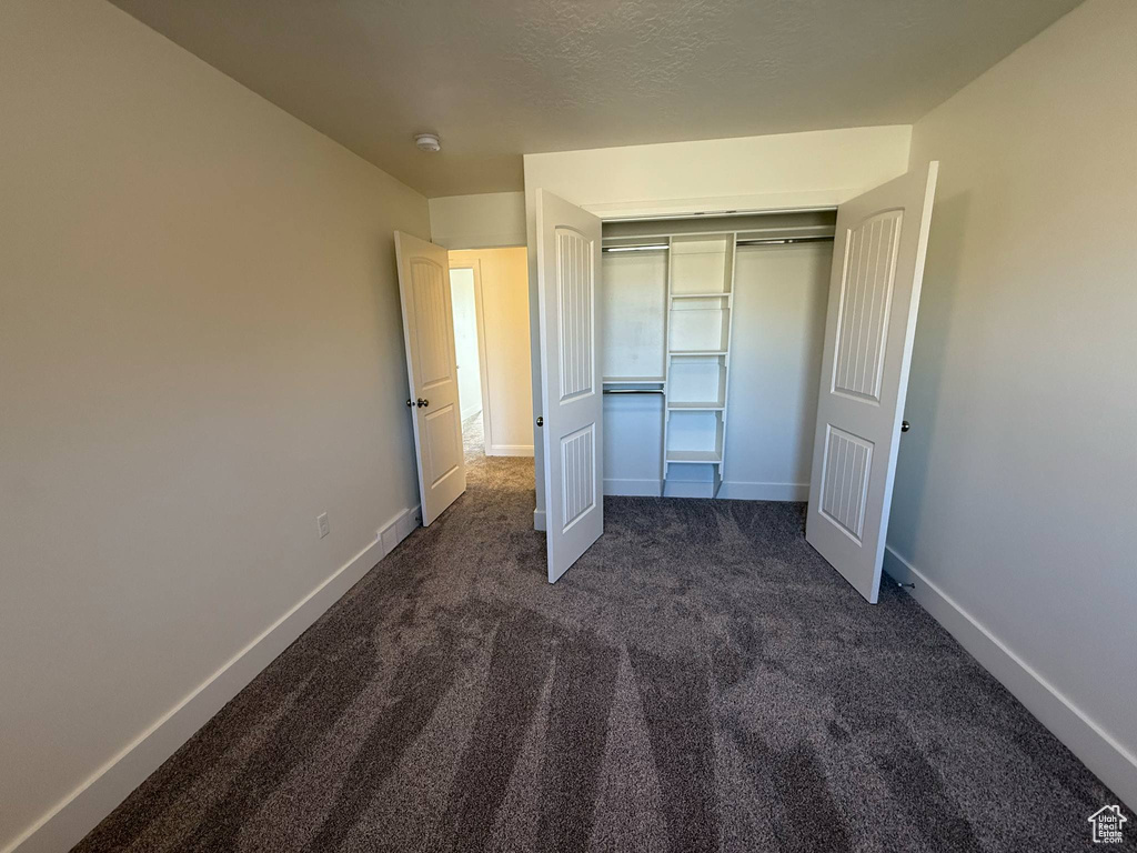 Unfurnished bedroom featuring dark colored carpet, baseboards, and a closet