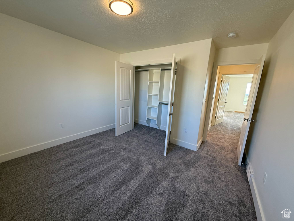 Unfurnished bedroom with dark colored carpet, a textured ceiling, baseboards, and a closet