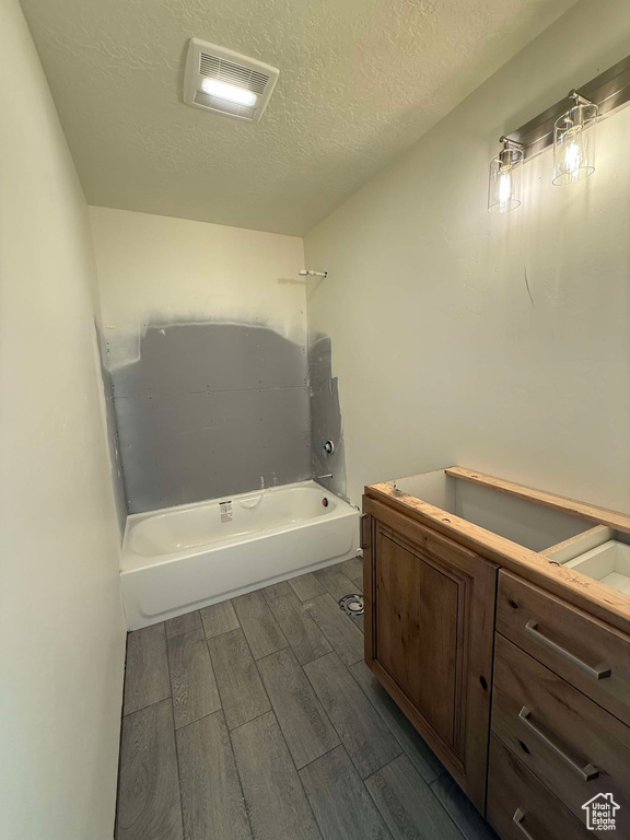 Bathroom with wood finish floors, visible vents, a textured ceiling, bathtub / shower combination, and vanity