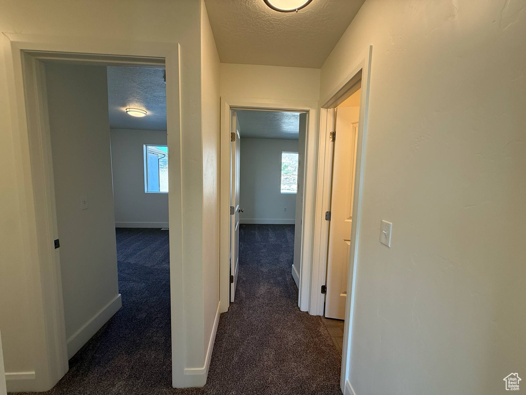 Hall with a textured ceiling, dark colored carpet, and baseboards