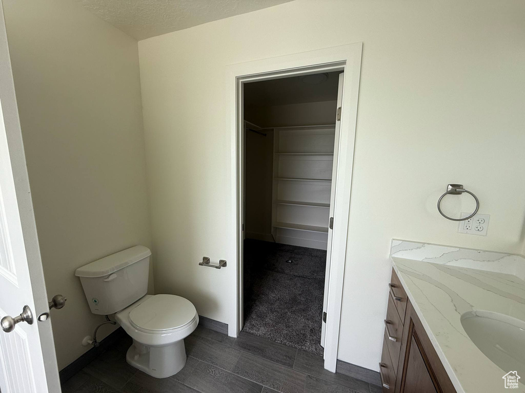 Bathroom featuring toilet, vanity, wood finished floors, and a walk in closet