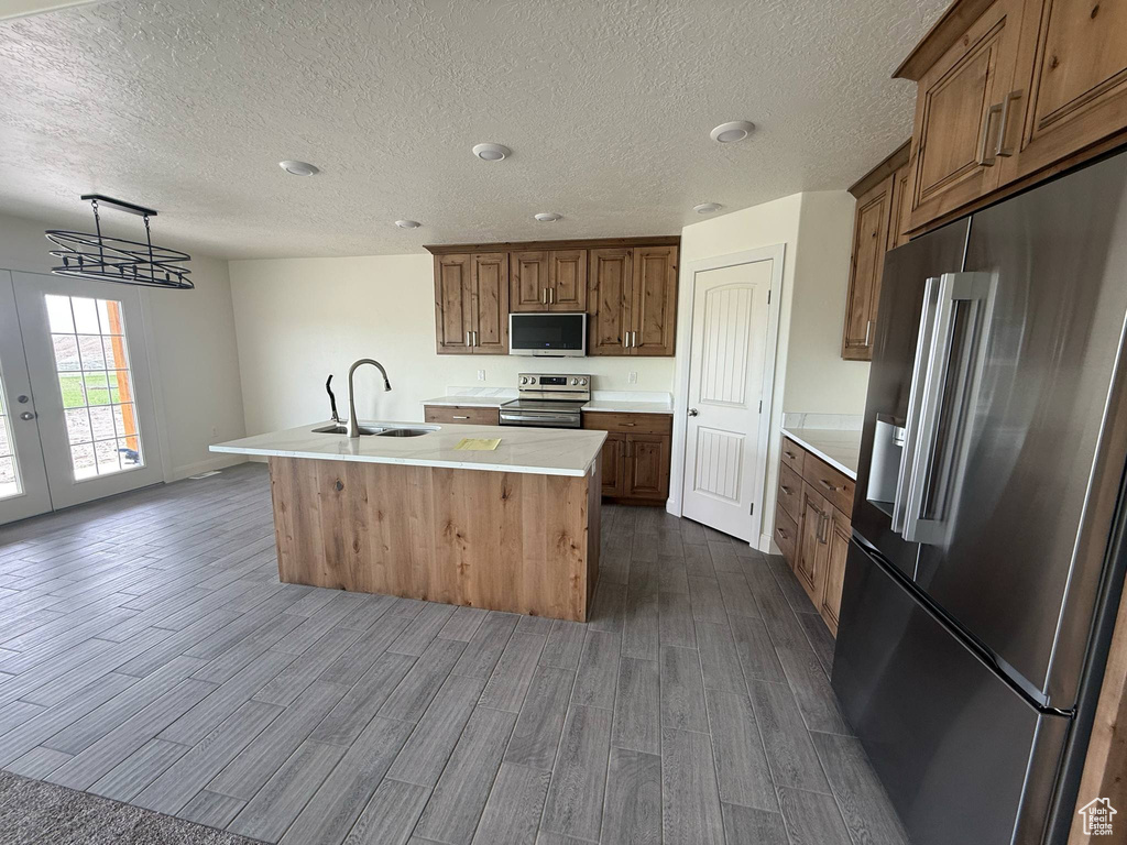 Kitchen featuring stainless steel appliances, a sink, dark wood-style flooring, an island with sink, and light countertops