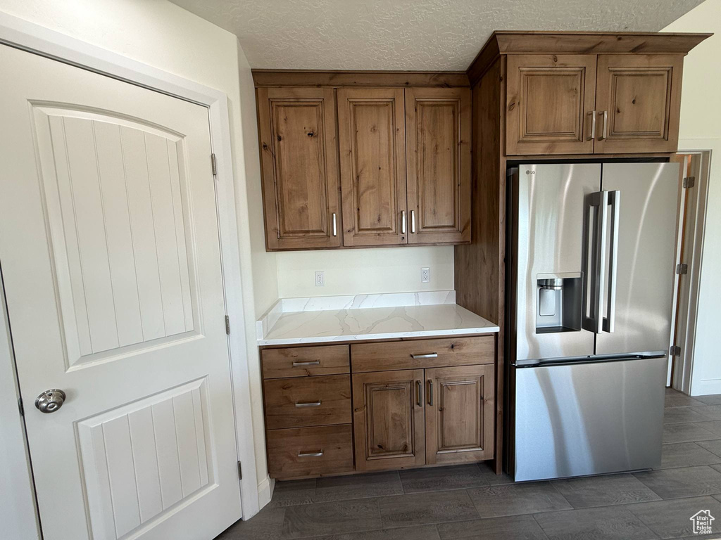 Kitchen featuring stainless steel fridge, brown cabinets, a textured ceiling, and light stone countertops