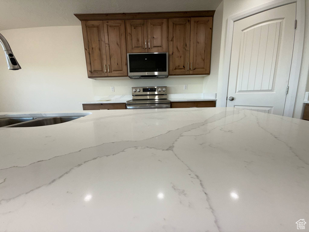 Kitchen featuring appliances with stainless steel finishes, a sink, and light stone countertops