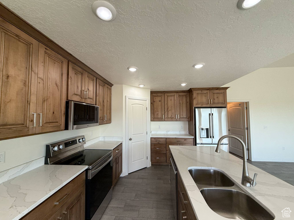 Kitchen with appliances with stainless steel finishes, a sink, dark wood finished floors, a textured ceiling, and light stone countertops