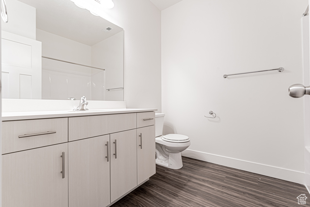 Full bathroom with vanity, toilet, wood finished floors, baseboards, and a shower