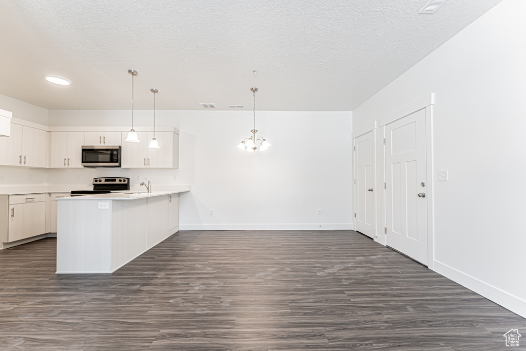 Kitchen with stainless steel appliances, a peninsula, baseboards, a chandelier, and a textured ceiling