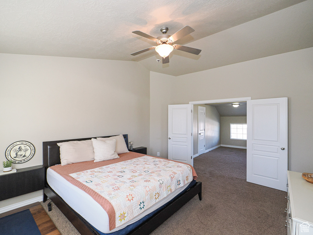 Carpeted bedroom with vaulted ceiling, ceiling fan, and a textured ceiling