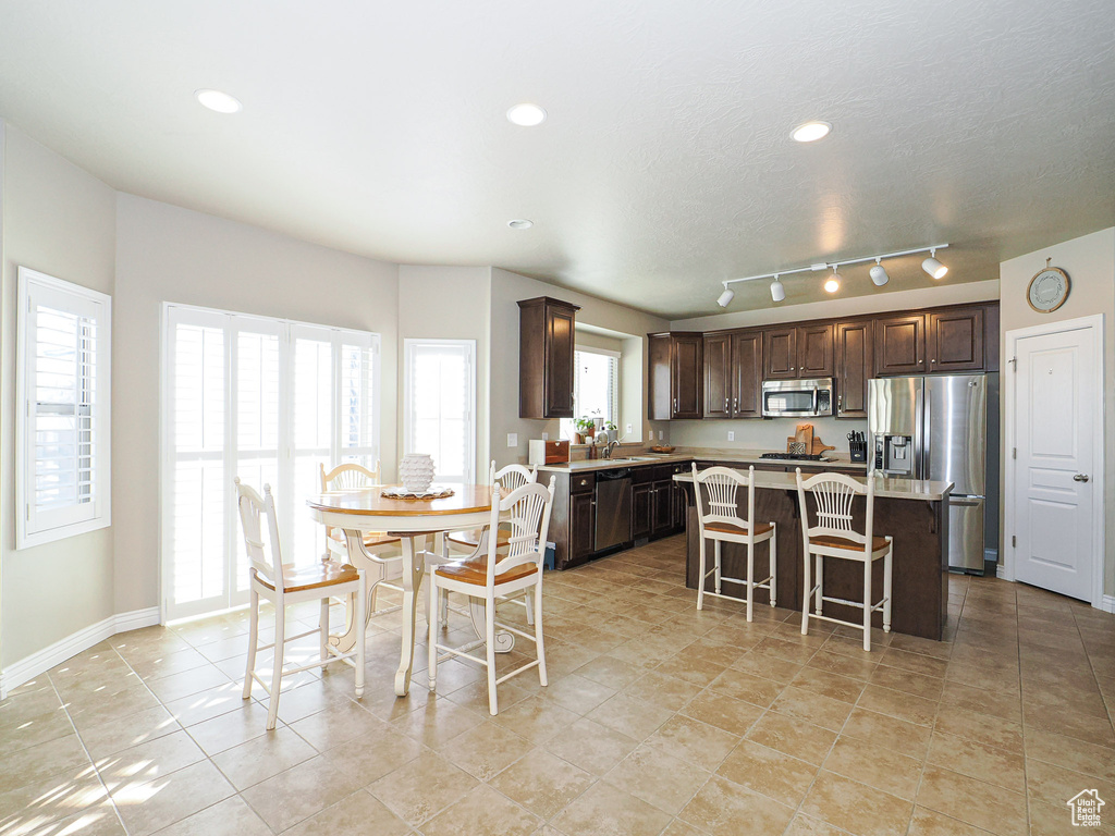 Kitchen featuring a kitchen bar, stainless steel appliances, a kitchen island, dark brown cabinetry, and sink