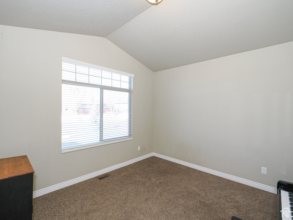 Carpeted spare room featuring lofted ceiling and heating unit