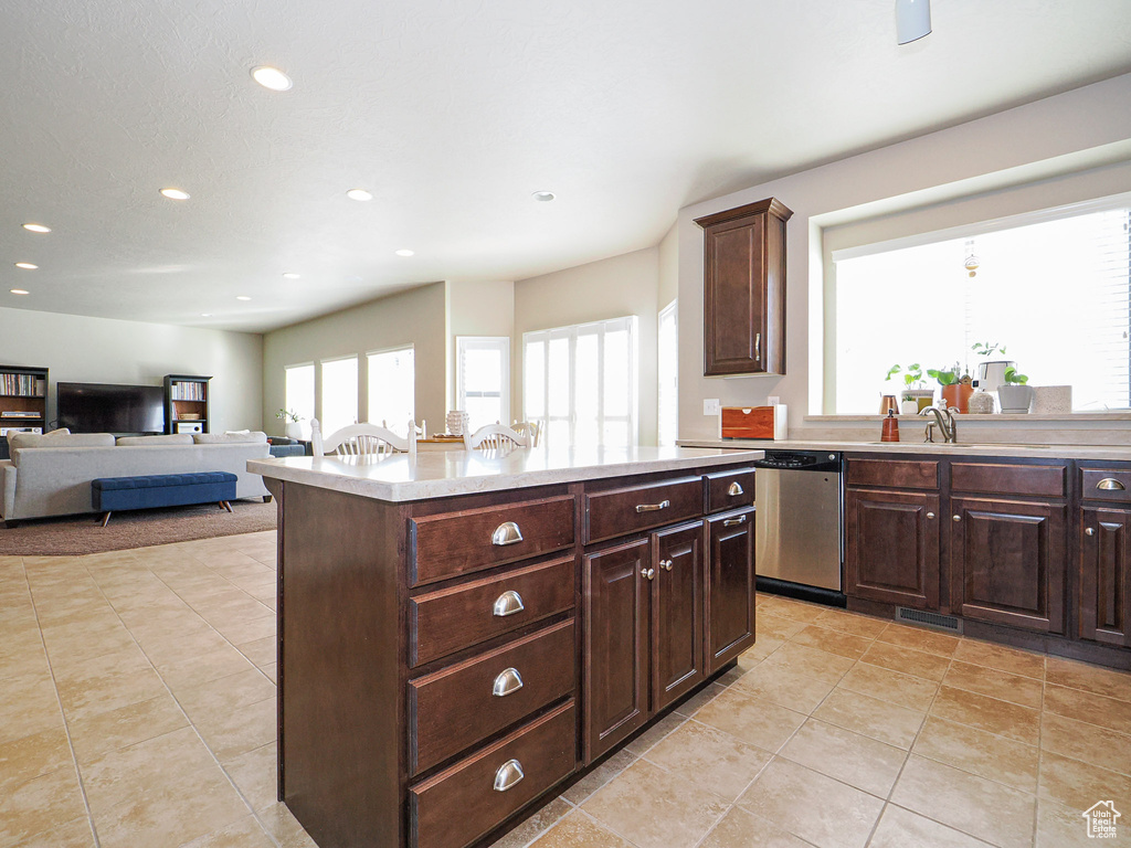 Kitchen with dark brown cabinetry, light tile patterned floors, dishwasher, and a kitchen island