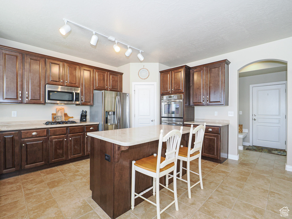 Kitchen with a center island, a kitchen bar, dark brown cabinetry, stainless steel appliances, and light tile patterned floors