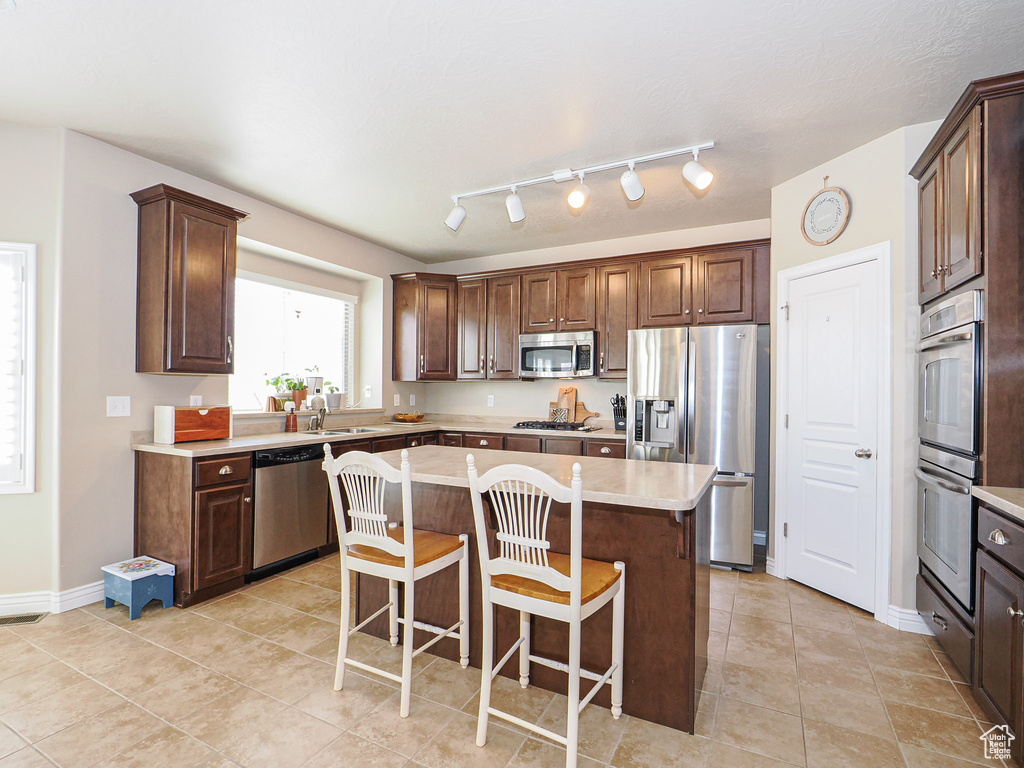 Kitchen featuring a center island, sink, dark brown cabinetry, appliances with stainless steel finishes, and a kitchen breakfast bar