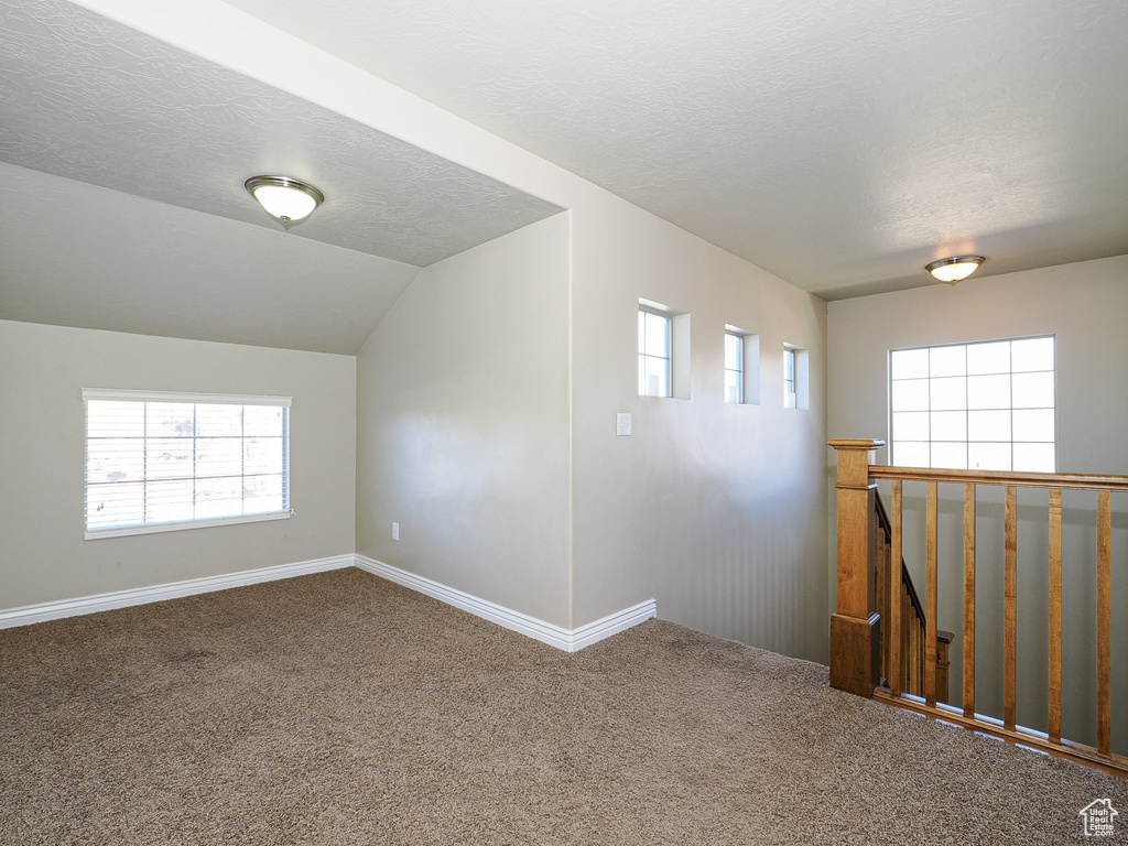 Carpeted empty room featuring a healthy amount of sunlight, vaulted ceiling, and a textured ceiling