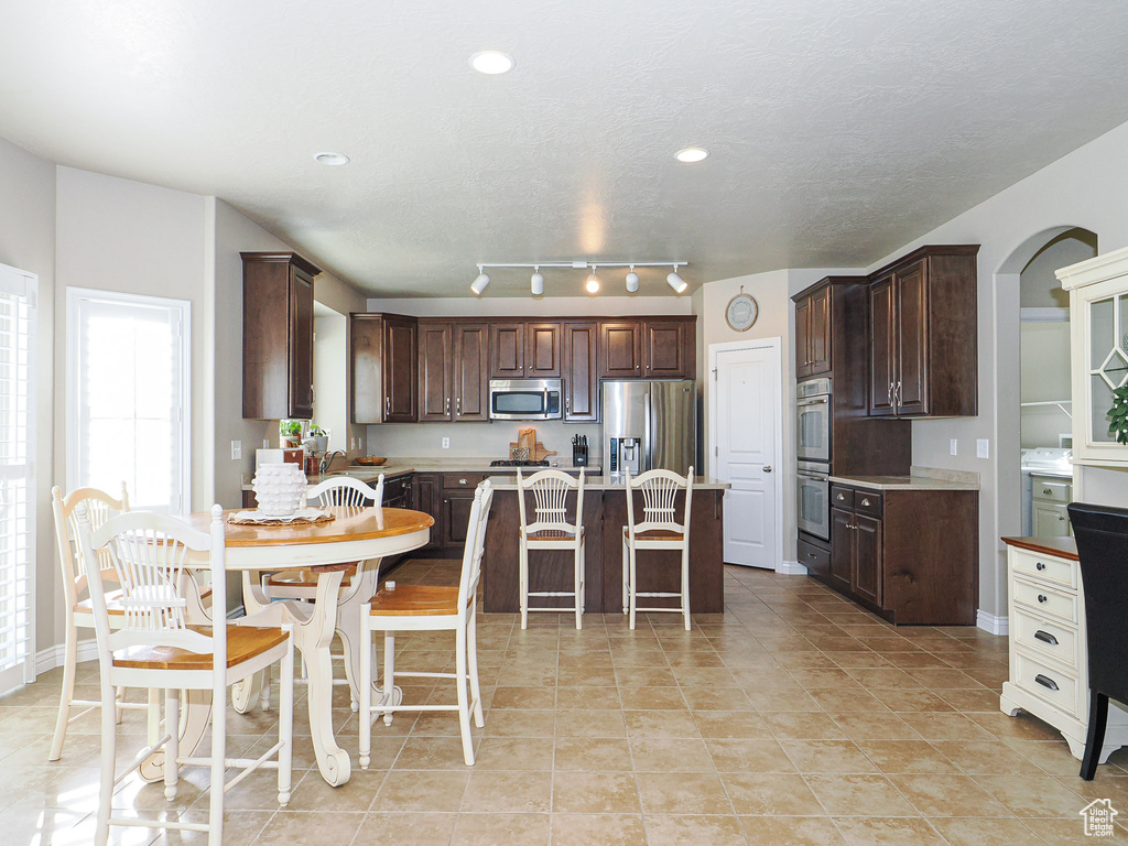 Kitchen featuring light tile patterned floors, stainless steel appliances, a kitchen breakfast bar, dark brown cabinetry, and a center island