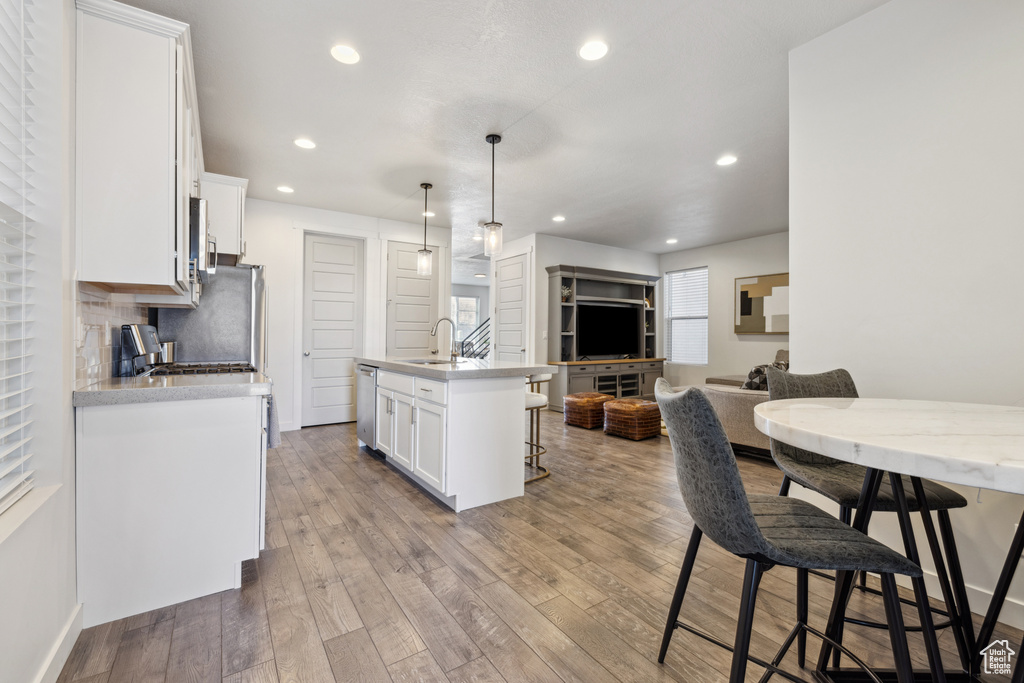 Kitchen featuring hardwood / wood-style flooring, a breakfast bar, stainless steel appliances, white cabinetry, and backsplash