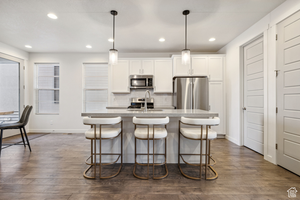 Kitchen featuring a center island with sink, stainless steel appliances, backsplash, a sink, and a kitchen bar