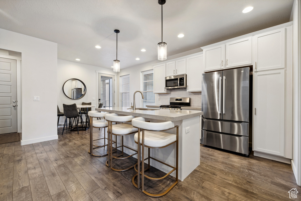 Kitchen with dark wood-style floors, appliances with stainless steel finishes, a center island with sink, and decorative backsplash