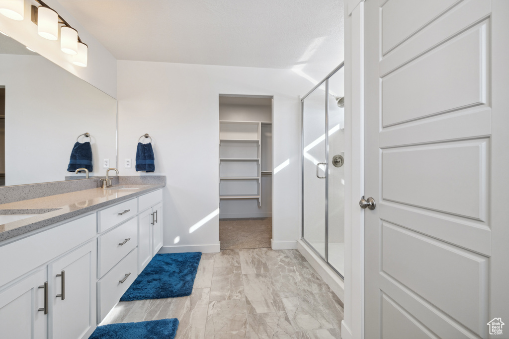 Full bath with double vanity, a shower stall, a spacious closet, and a sink