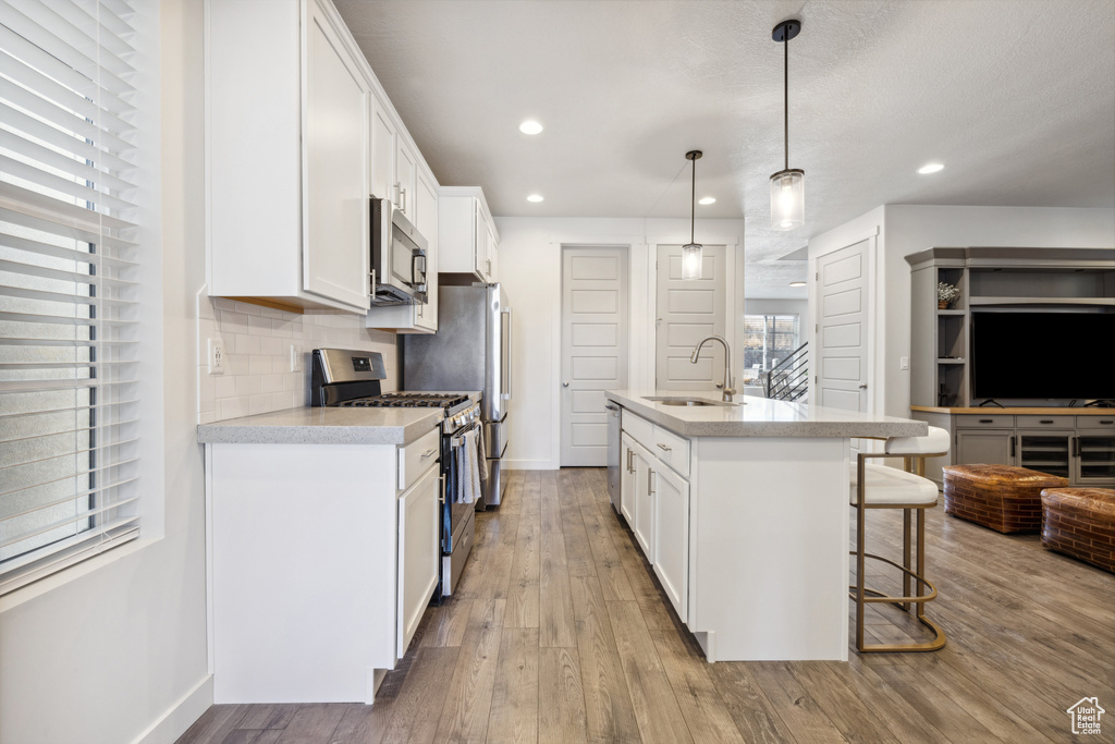 Kitchen featuring a breakfast bar, a sink, appliances with stainless steel finishes, tasteful backsplash, and wood-type flooring