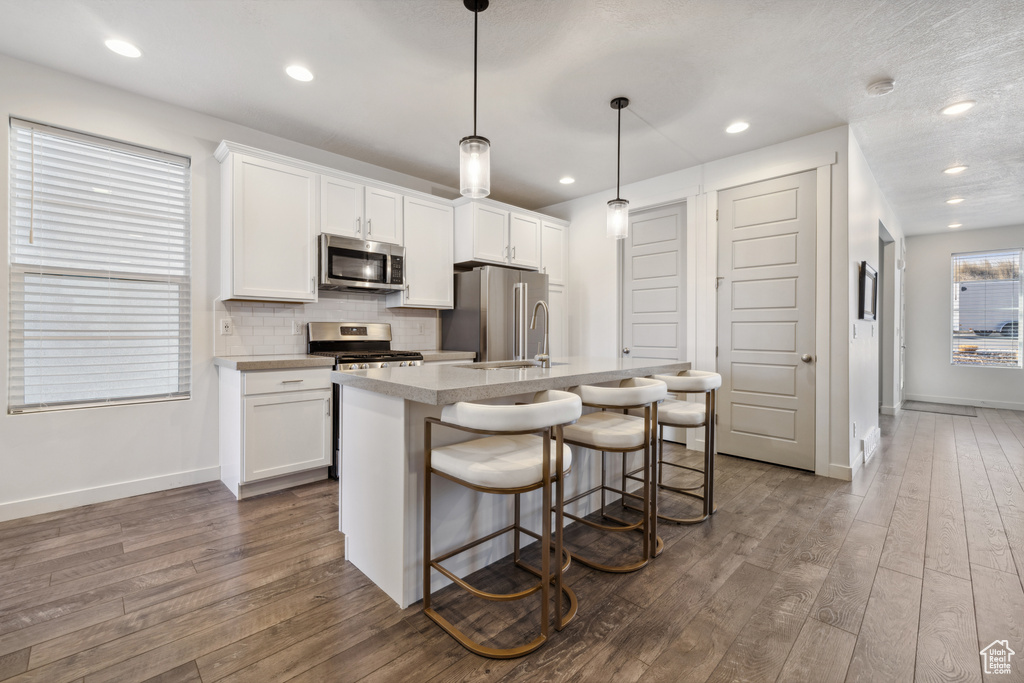 Kitchen with tasteful backsplash, a center island with sink, dark wood finished floors, stainless steel appliances, and white cabinetry