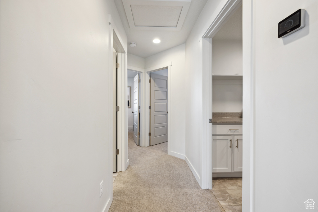 Corridor with attic access, baseboards, and light colored carpet