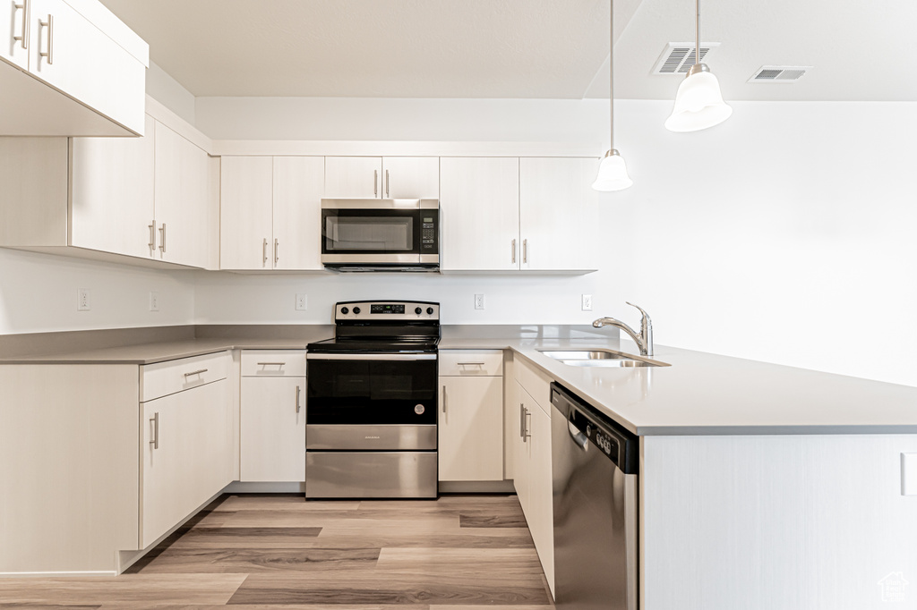 Kitchen with appliances with stainless steel finishes, a sink, light wood-type flooring, a peninsula, and light countertops