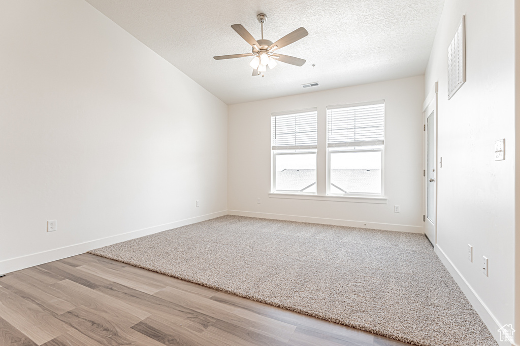 Empty room with wood finished floors, ceiling fan, a textured ceiling, baseboards, and lofted ceiling