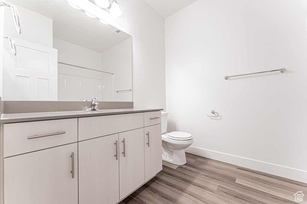 Bathroom with vanity, toilet, baseboards, wood finished floors, and a shower