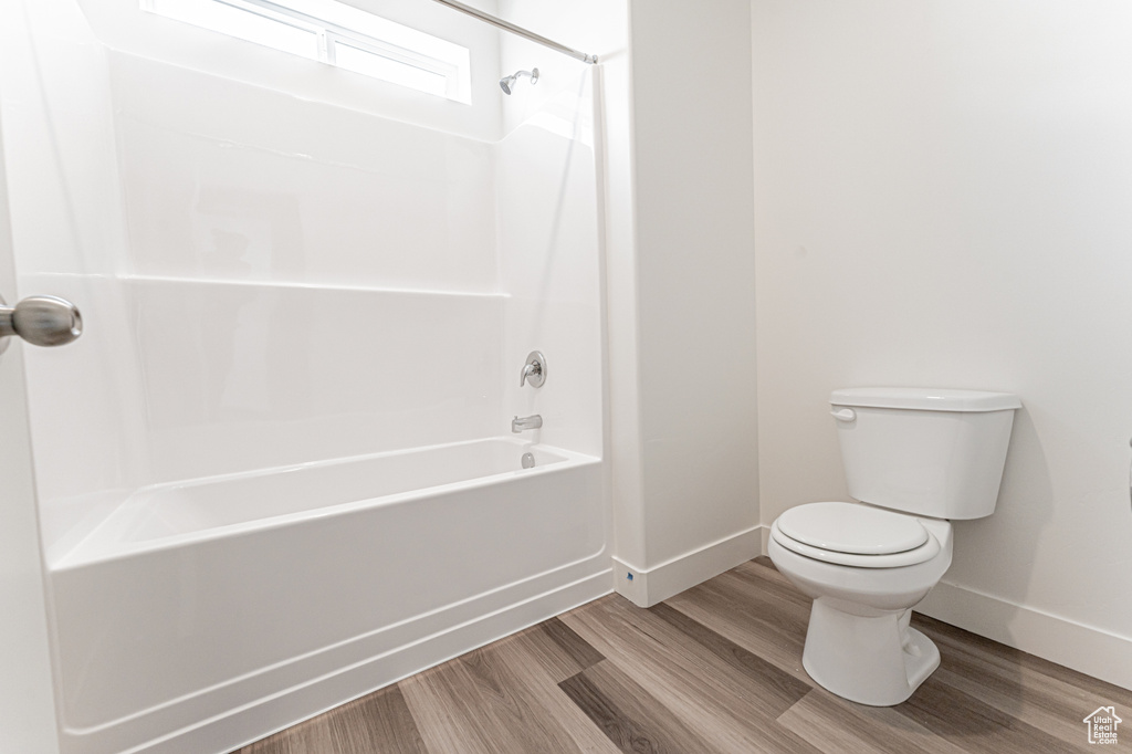 Bathroom featuring baseboards, wood finished floors, toilet, and shower / bath combination