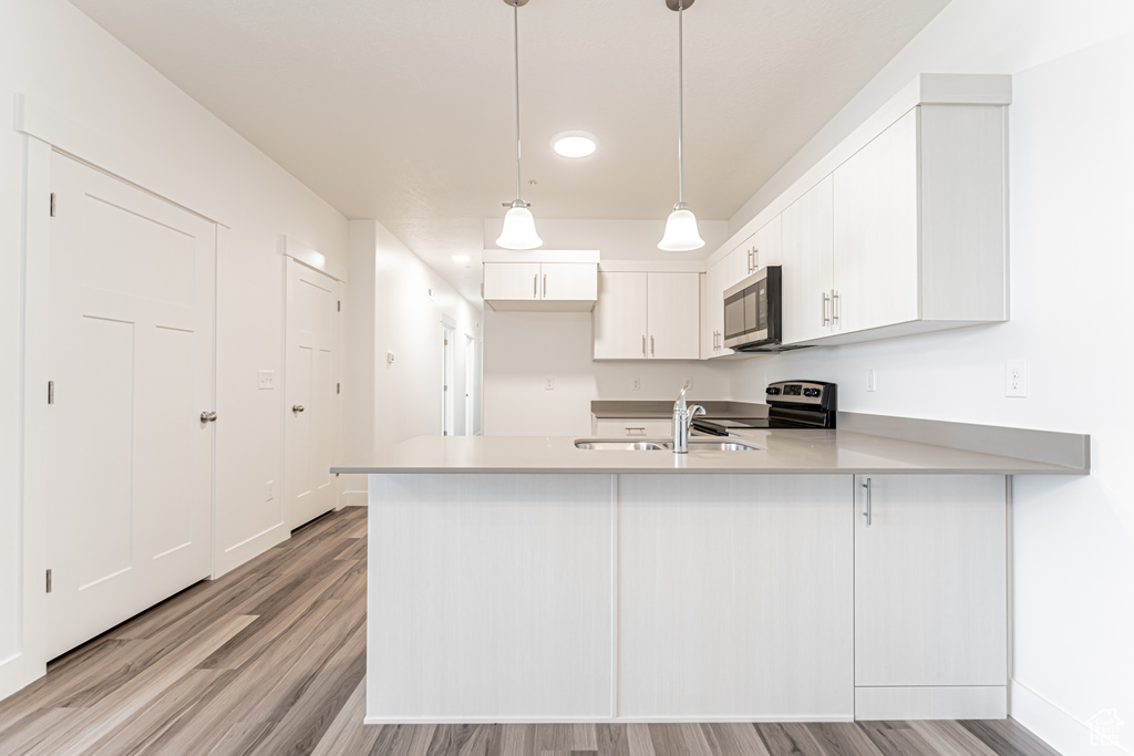 Kitchen featuring stainless steel appliances, a peninsula, a sink, light wood finished floors, and light countertops