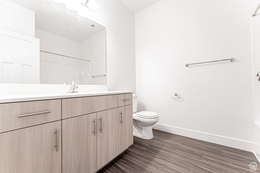 Bathroom with vanity, baseboards, toilet, wood finished floors, and a shower