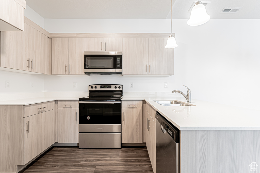 Kitchen featuring stainless steel appliances, a sink, a peninsula, light brown cabinets, and light countertops