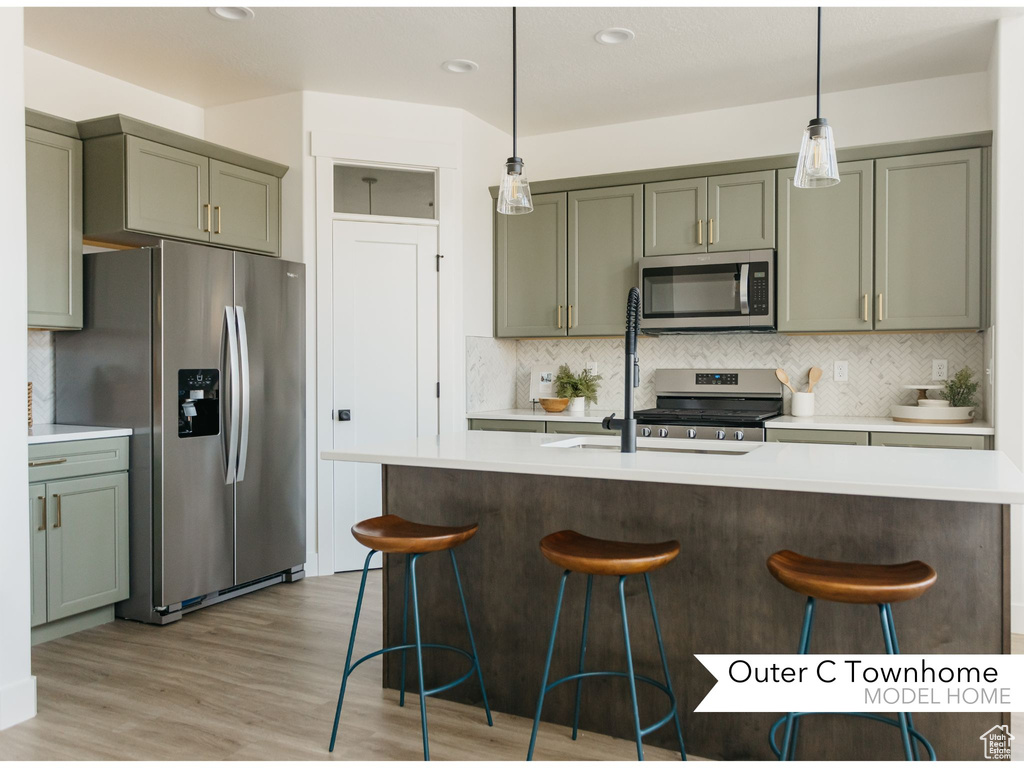 Kitchen featuring light hardwood / wood-style floors, appliances with stainless steel finishes, decorative light fixtures, backsplash, and a breakfast bar area