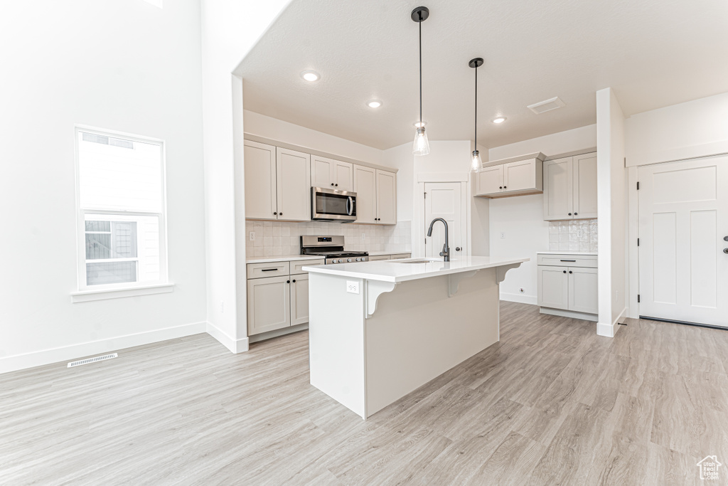 Kitchen featuring light wood-style floors, appliances with stainless steel finishes, light countertops, backsplash, and a sink