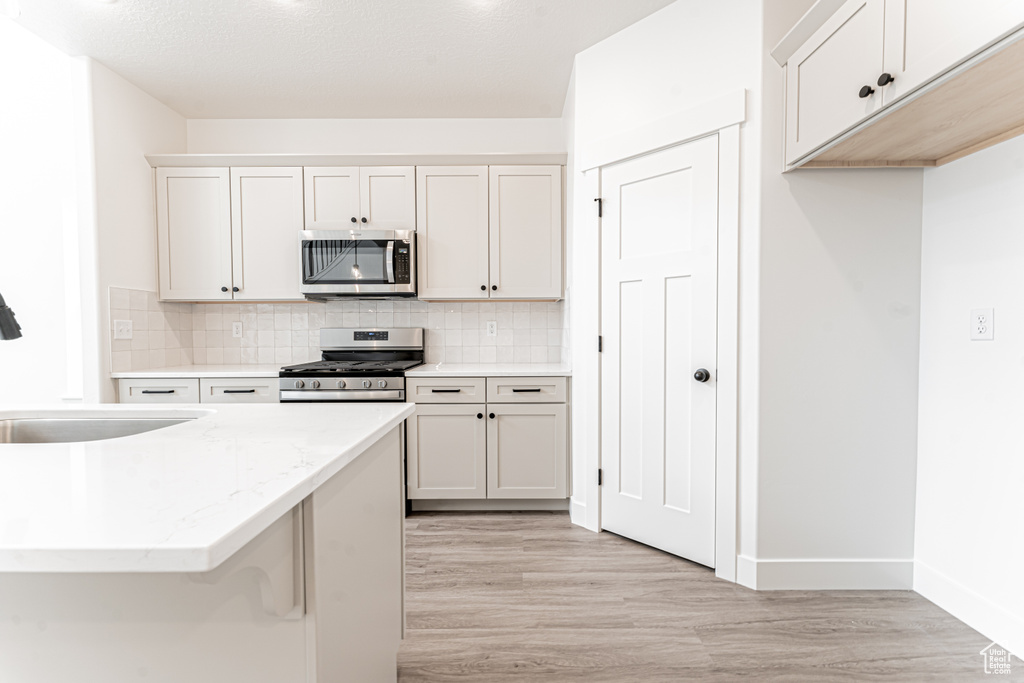 Kitchen featuring baseboards, tasteful backsplash, stainless steel appliances, and light wood-type flooring