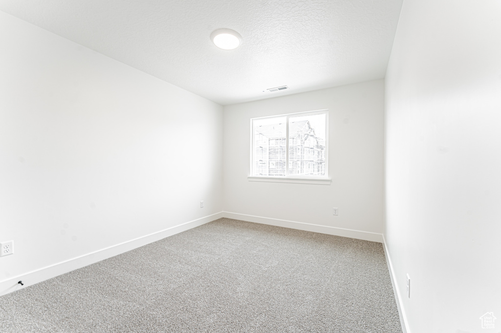 Empty room with baseboards, visible vents, a textured ceiling, and light colored carpet