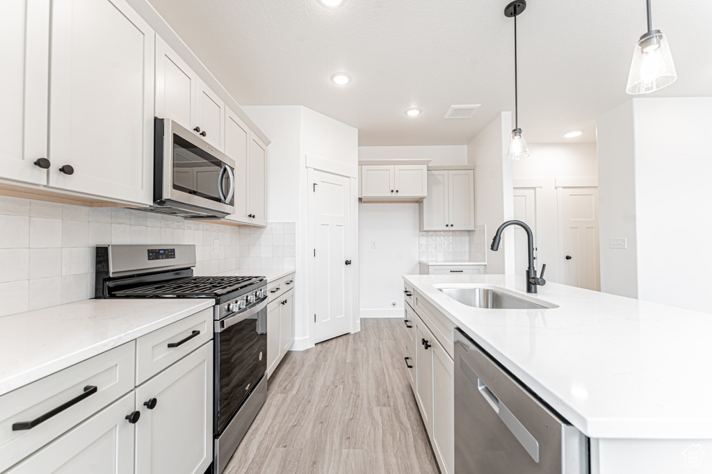 Kitchen with a sink, appliances with stainless steel finishes, light wood-type flooring, an island with sink, and backsplash