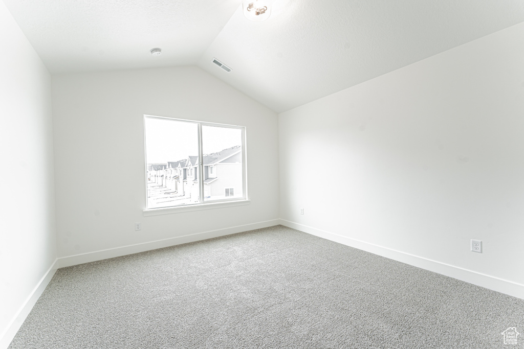 Carpeted empty room featuring baseboards, visible vents, and lofted ceiling