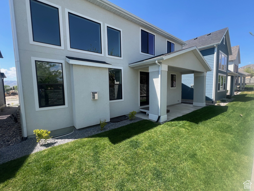 Rear view of house with stucco siding, a yard, and a patio area